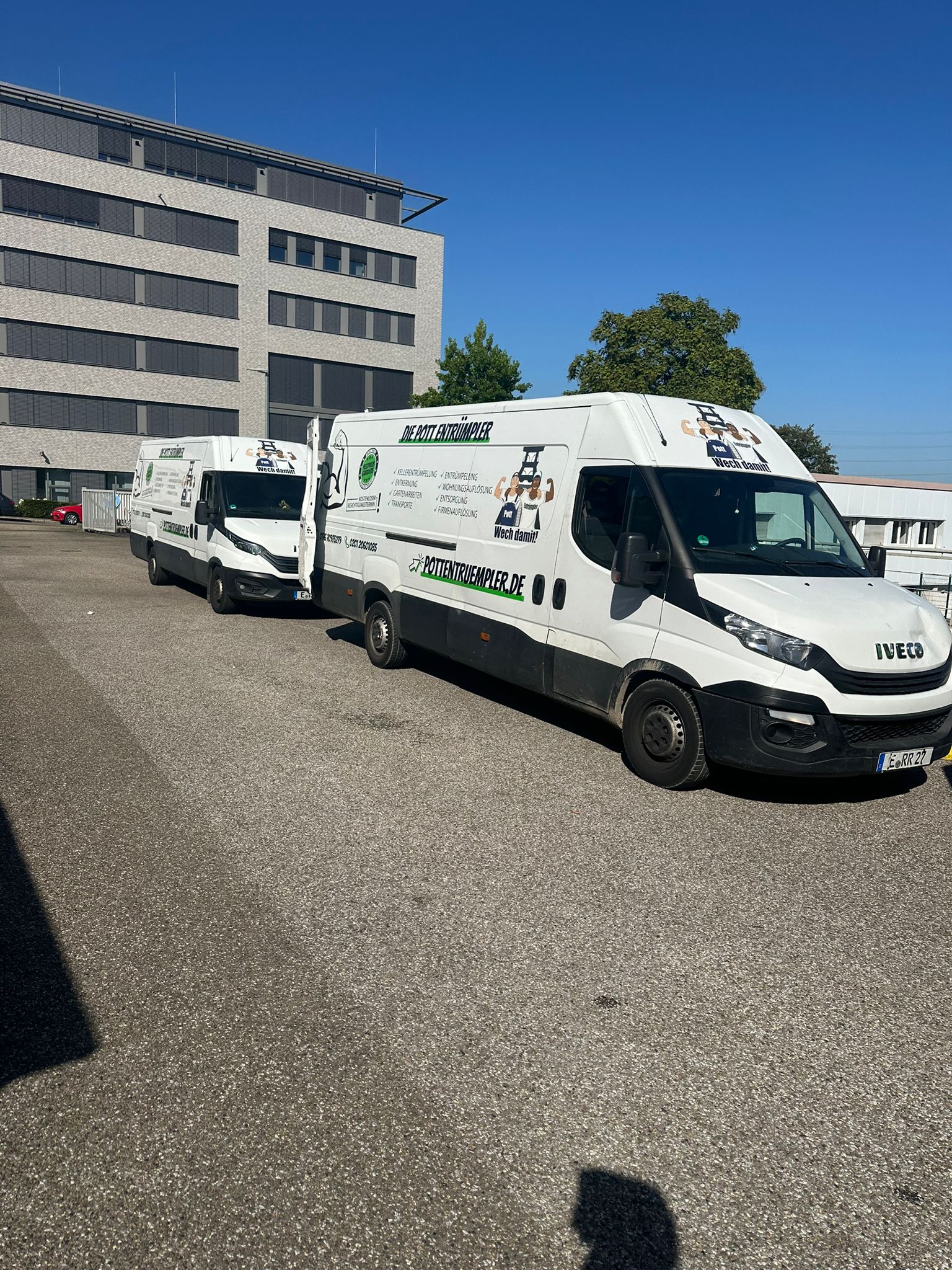 Zwei weiße Kleintransporter mit Firmenwerbung an den Seiten parken unter blauem Himmel auf einem Parkplatz neben einem modernen Bürogebäude. Zwei weiße Kleintransporter mit Firmenwerbung an den Seiten parken unter blauem Himmel auf einem Parkplatz neben einem modernen Bürogebäude.